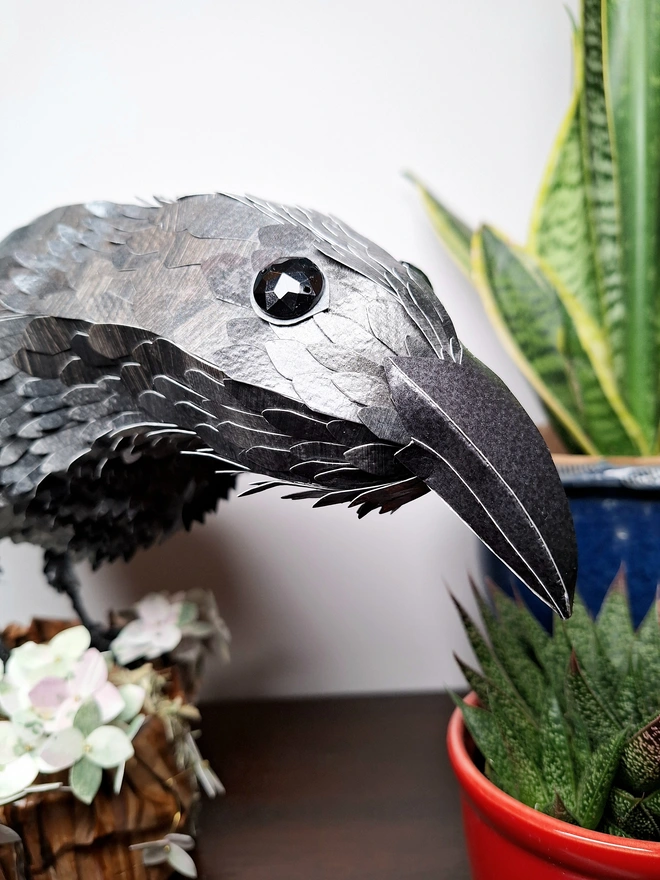 Close up of a paper sculpture of a raven perch3d on a tree stump