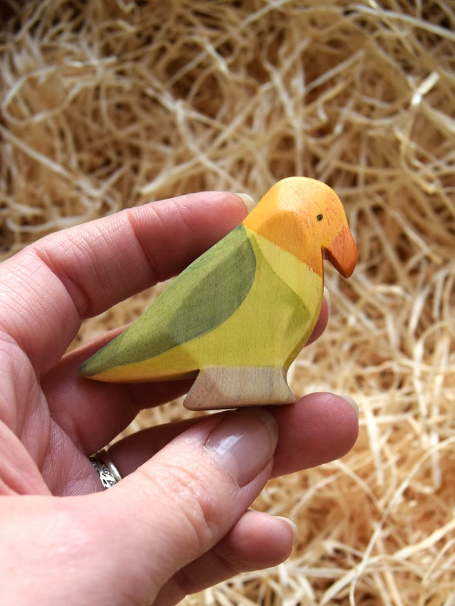 lovebird wooden toy held in hand above woodwool