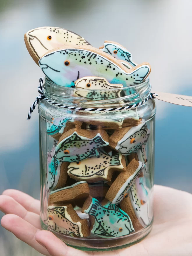 A joyful jar of fish biscuits seen held by someone