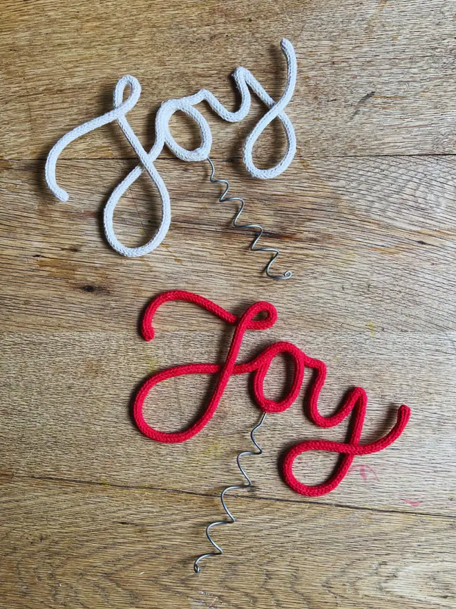 Two Christmas tree toppers spelling "Joy" in cursive against an oak table top