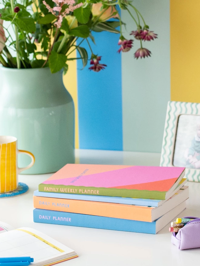 Colourful planners from the Raspberry Blossom Happiness stationery collection sit in a pile on a desk