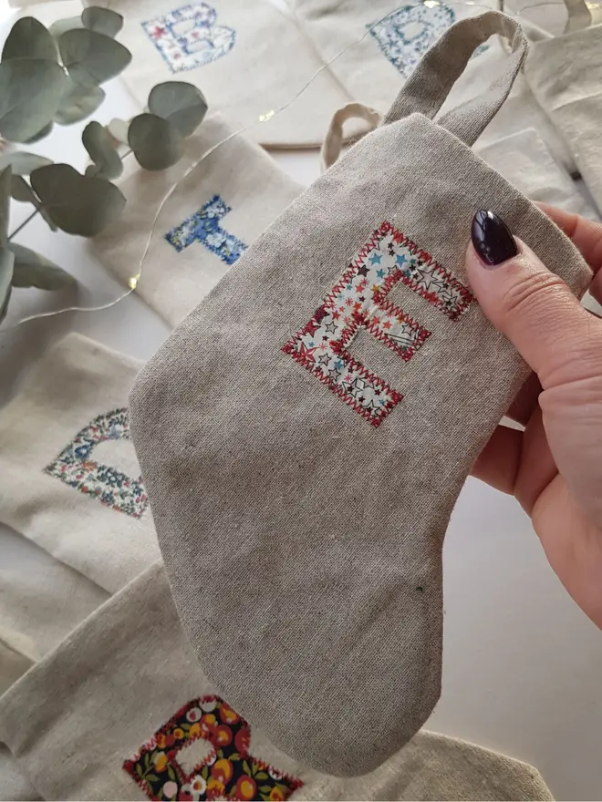 Floral Linen Christmas Stocking. Natural Linen Stocking in a hand with a floral letter E 
