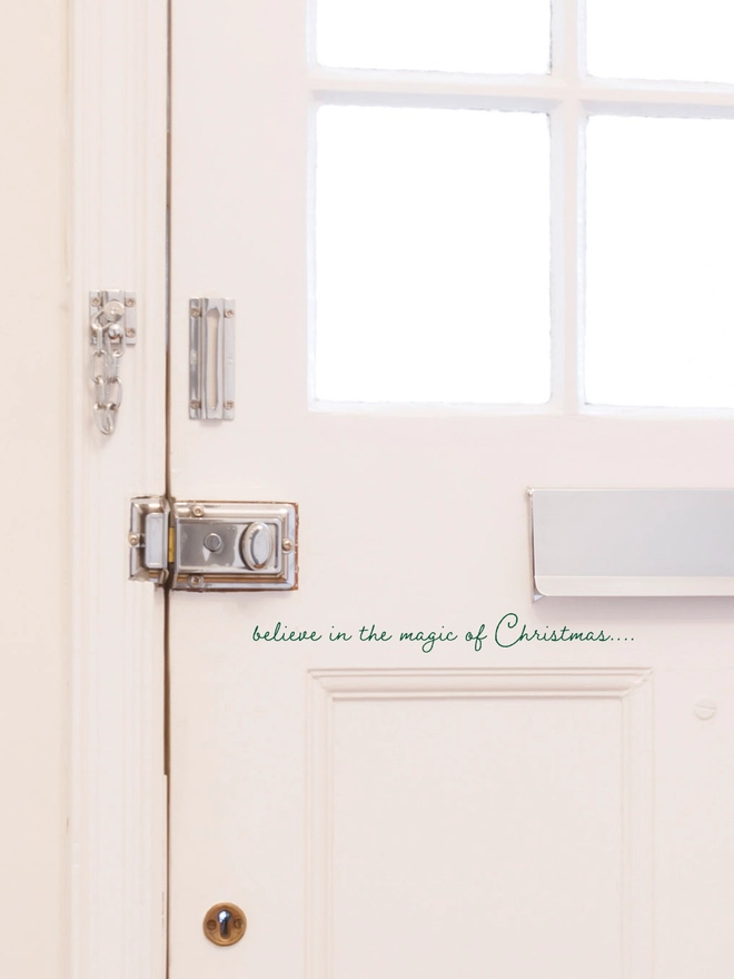 White front door with a letter box and a sticker which says believe in the magic of christmas