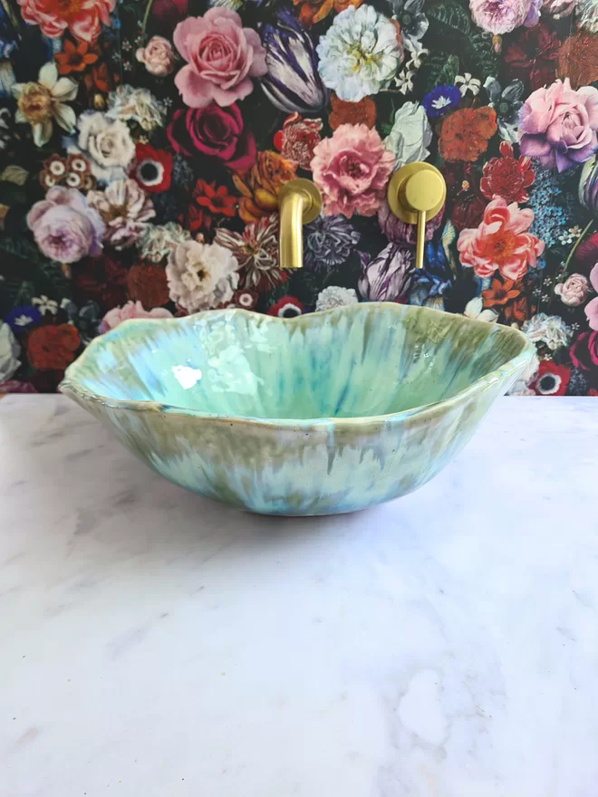 Handcrafted ceramic bathroom basin in a turquoise green blue glaze, hand-crafted sink, pottery basin, wc, bathroom, ensuite, modern bathroom, photographed against colourful floral wallpaper with gold taps, homeware, interiors, front view