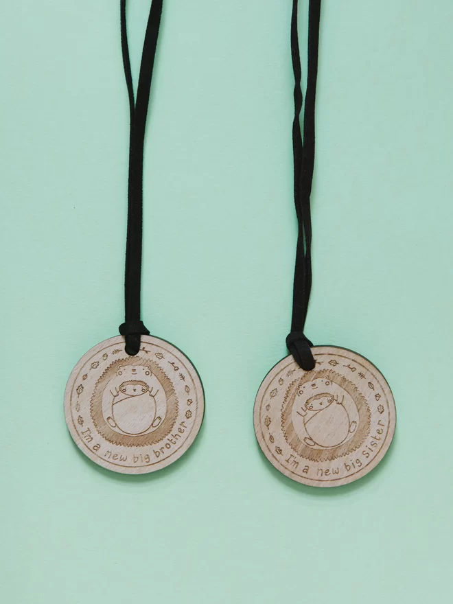 2 wooden medals for new big siblings. The medals are etched with a drawing of a hedgehog holding a baby hedgehog