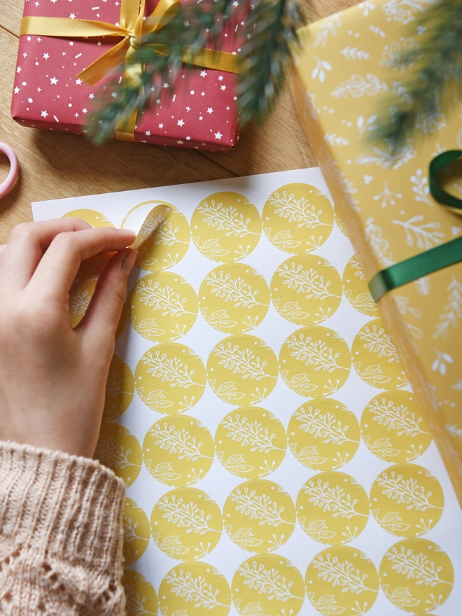 A round yellow sticker with a gentle botanical design is being peeled from a sheet of 35 matching stickers.