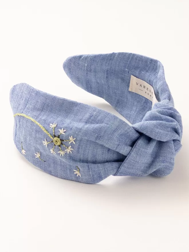 Amelie Headband in Fleur Flax Blue seen flat close with embroidered dandelions on the side and a top-knot tie.