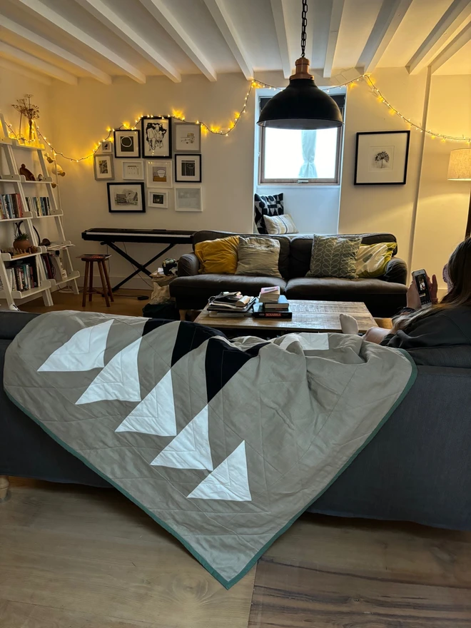 Flow Taupe Linen Throw Quilt. A natural quilt with bold triangle pattern. Throw quilt draped on sofa.