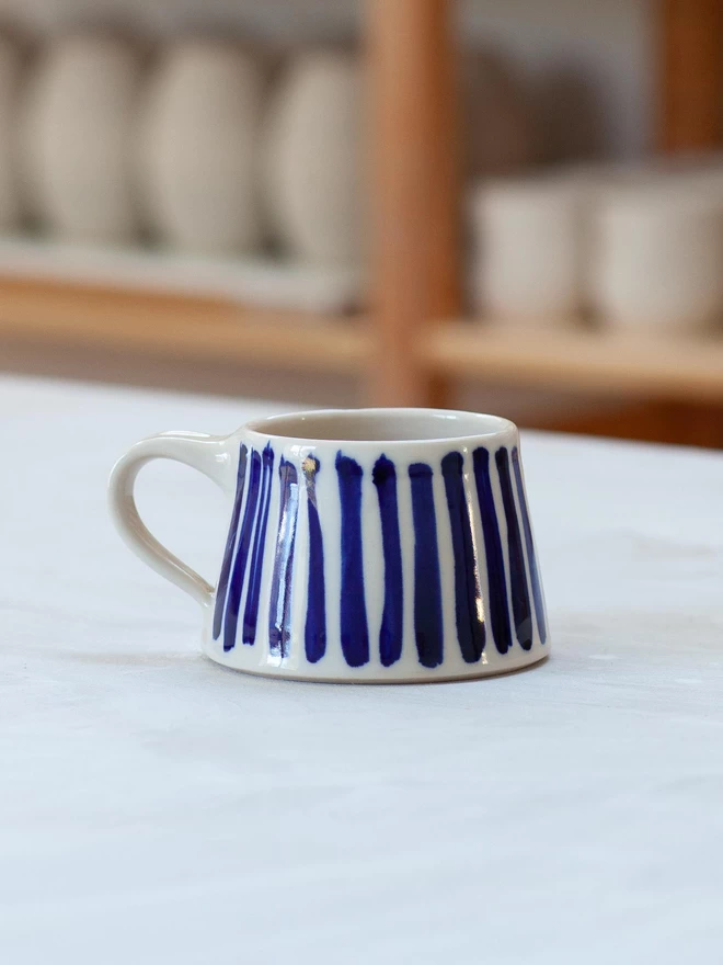 Gloss handmade mug with cobalt blue hand-painted stripes with blurred studio pots in background