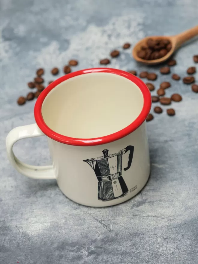 Picture of a Cream Enamel Mug with a Red Rim with a Moka Pot design etched onto it, taken from an original Lino Print