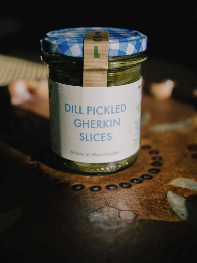 Jar Of Dill Pickled Gherkin Slices, jar of gherkin slices with a blue lid on a decorated plate. 