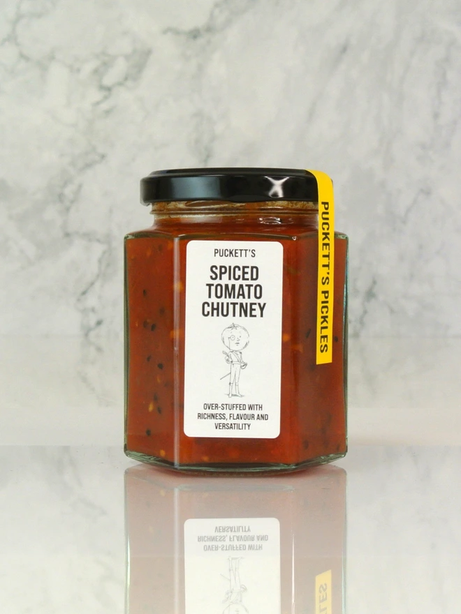 spiced tomato chutney. a jar of tomato chutney photographed on a marble background.