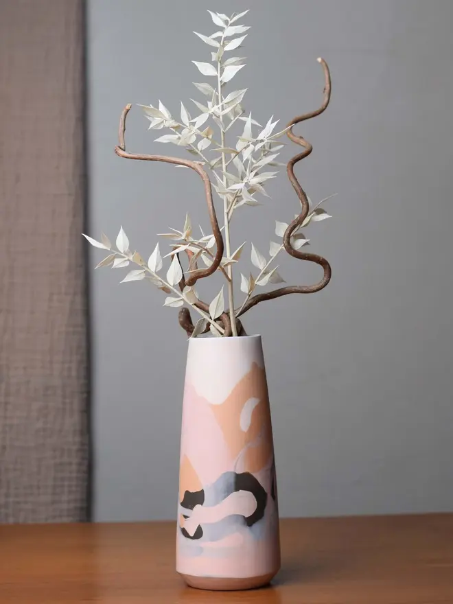 porcelain vase on table, vase has shades of orange, brown, and whites, and is holding dried foliage