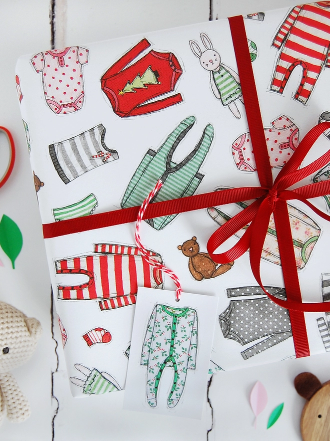 A gift wrapped in hand illustrated first Christmas wrapping paper with tiny baby clothes printed all over.