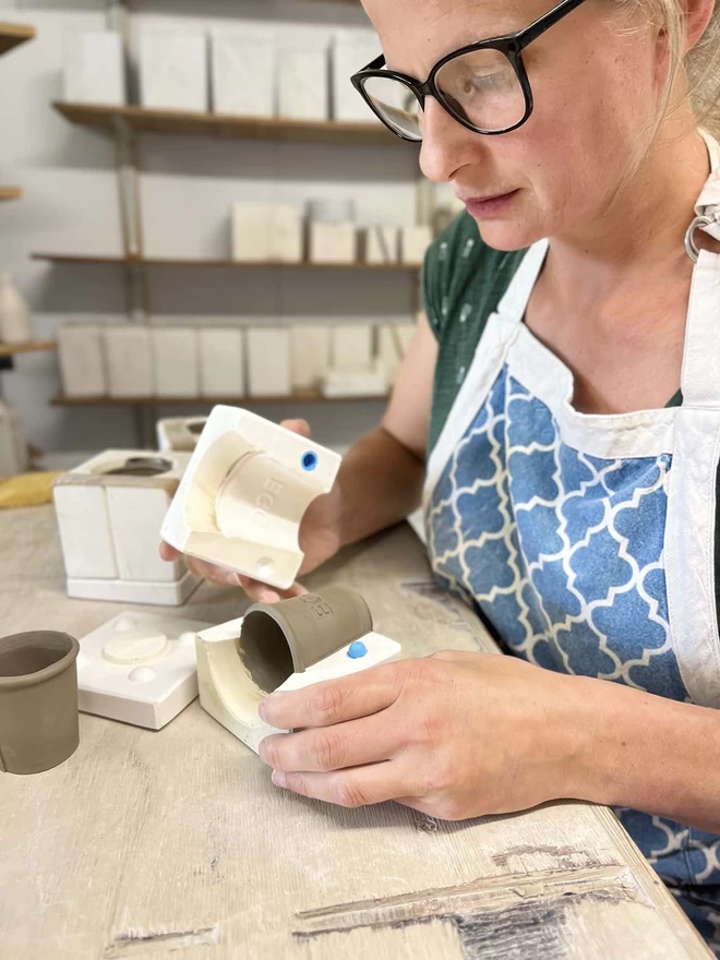 Katie removing one part of a plaster mould, showing a freshly cast clay egg cup nestled inside.
