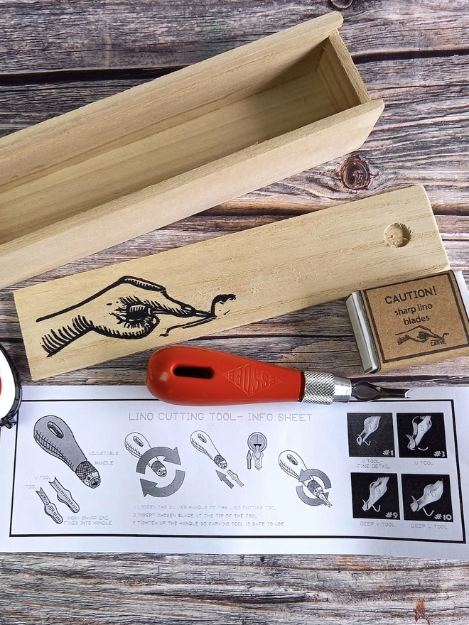 Lino Carving Printing Tool Kit In Presentation Box, carving utensils and instruction sheet unpacked on a wooden table. 