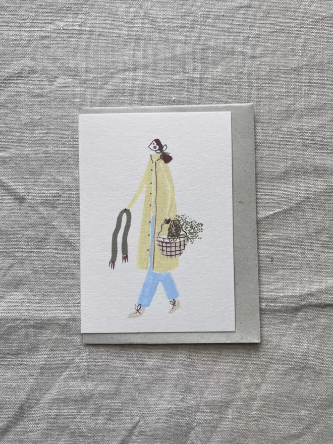 a greetings card with a girl in a yellow coat and carrying a basket. 