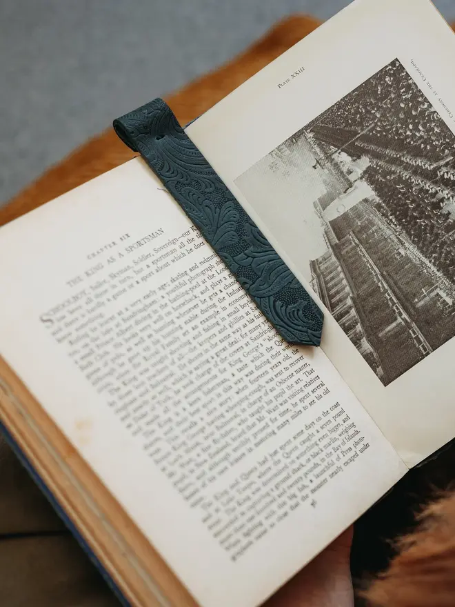 botanical leather bookmark. a dark green bookmark laid between two pages of a book.