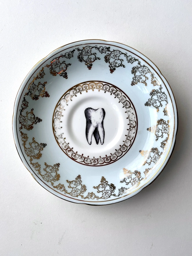 vintage plate with ornate border has a black and white image of a victorian molar tooth in the centre