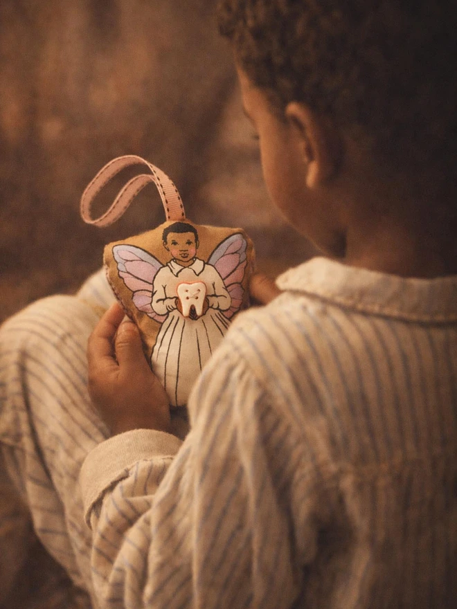 a little afro Caribbean boy in pj's holding an afro Caribbean tooth fairy boy doll
