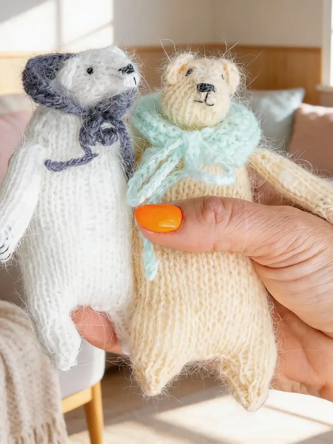 Ottilie The Bear Cashmere Figure, a pair of cashmere bears held by a person against a living room backdrop. 