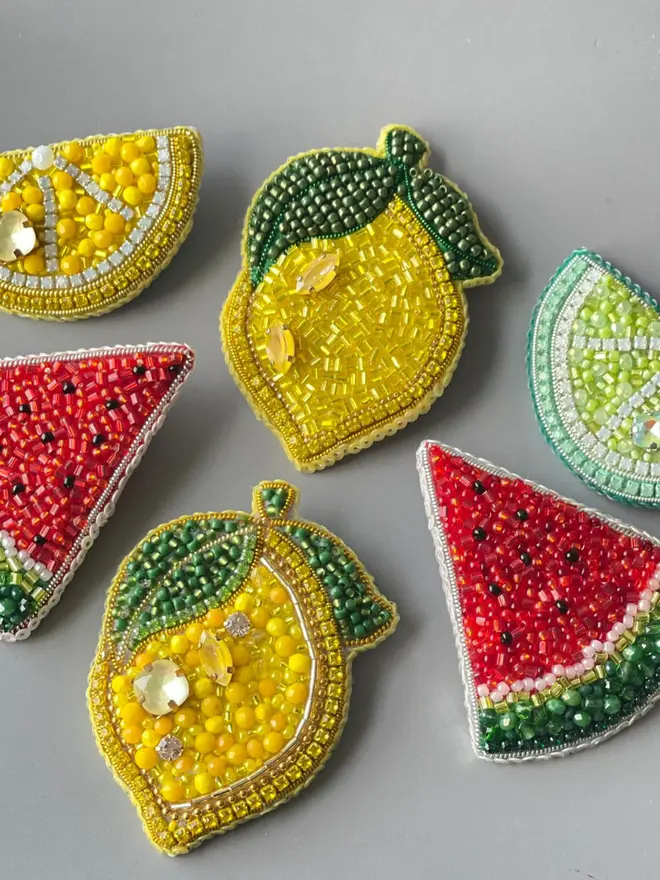 Lemon Beaded Brooch amongst other beaded fruit brooches, displayed on a plain background. 