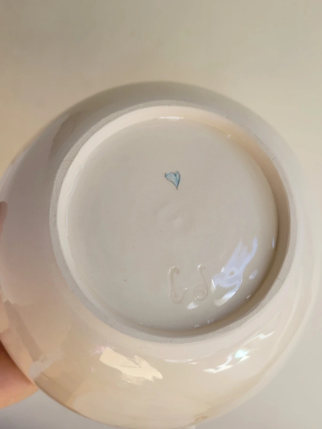 the underside of a cream pottery bowl with a small blue heart underneath