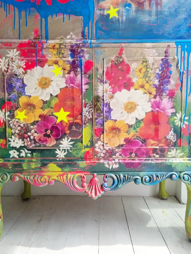 Upcycled cocktail cabinet in neons and bright colours. The decoration features a retro pin-up model on a boat and florals with stars and the wording reads ‘let your heart sing’