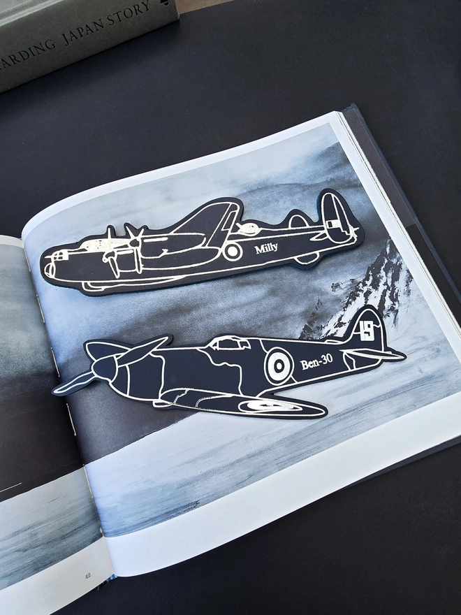 A navy blue leather bookmark of an Avro Lancaster war plane and a spitfire from World War Two on a book of landscape imagery