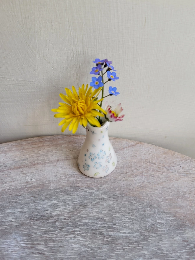forget me not miniature pottery vase on a wooden surface with daisy dandelion and forget me not inside 