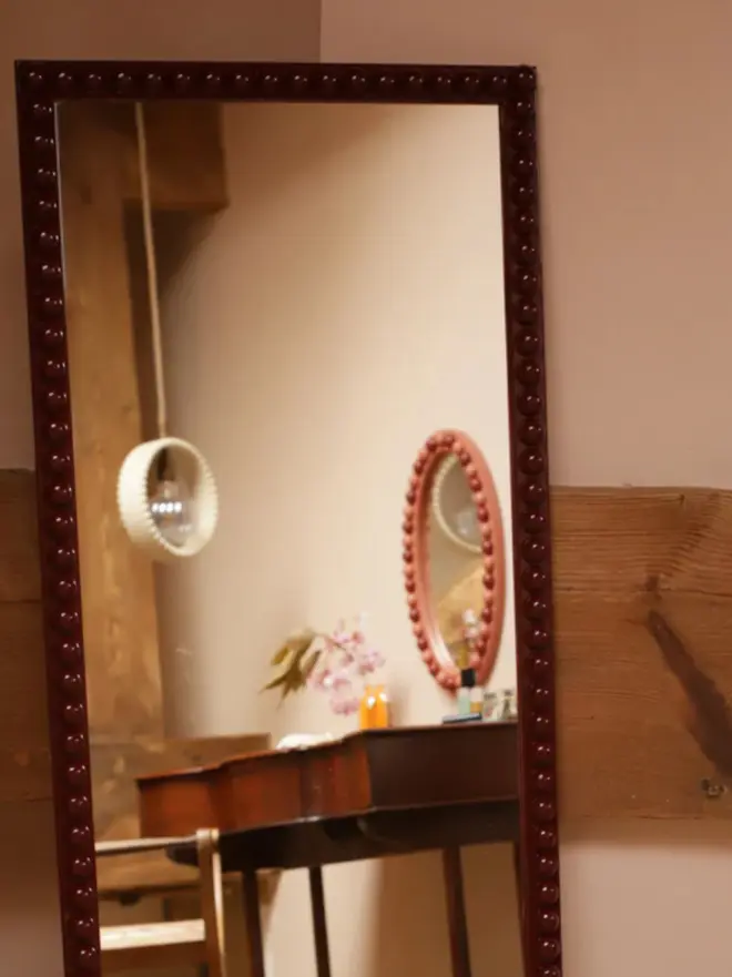 Floor-length bobbin mirror with a decorative turned-wood frame, placed in a classically decorated room with elegant furnishings.
