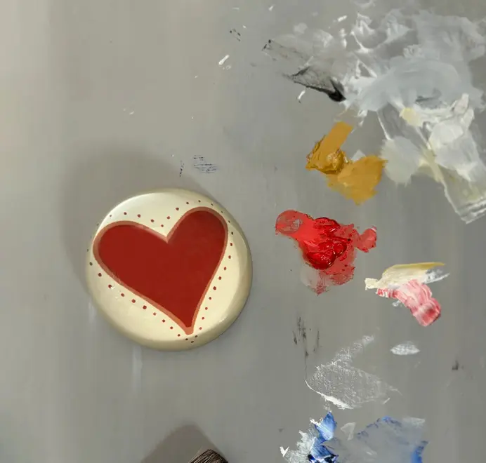 Round paperweight with a red heart on a painted grey background.