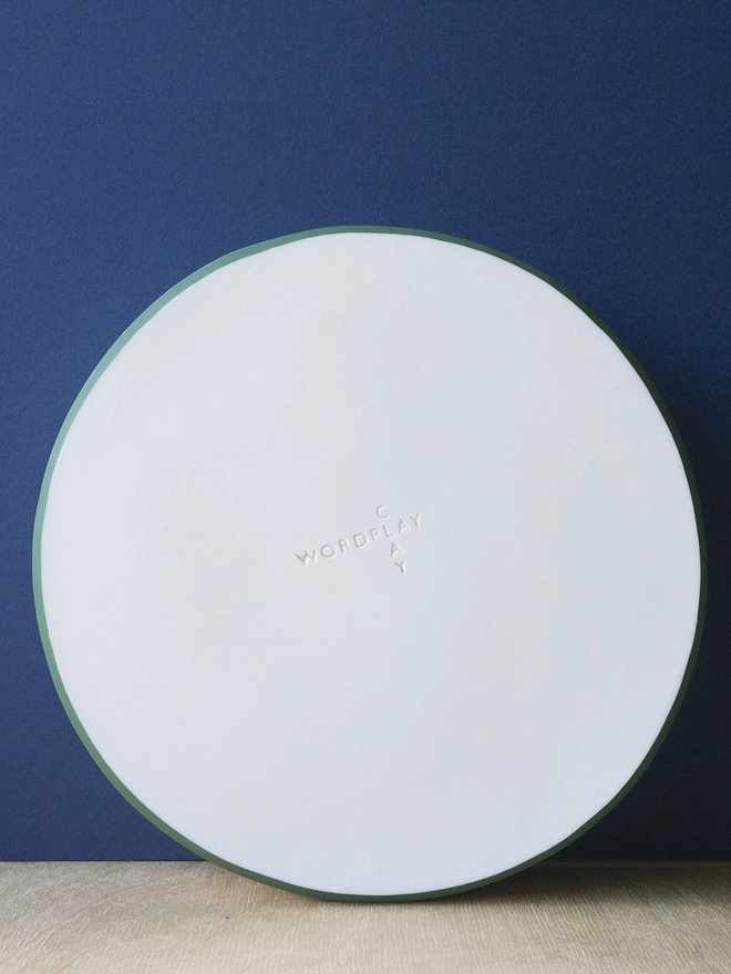 Ceramic porcelain dish with green rim and Wordplay Clay stamped into the base.