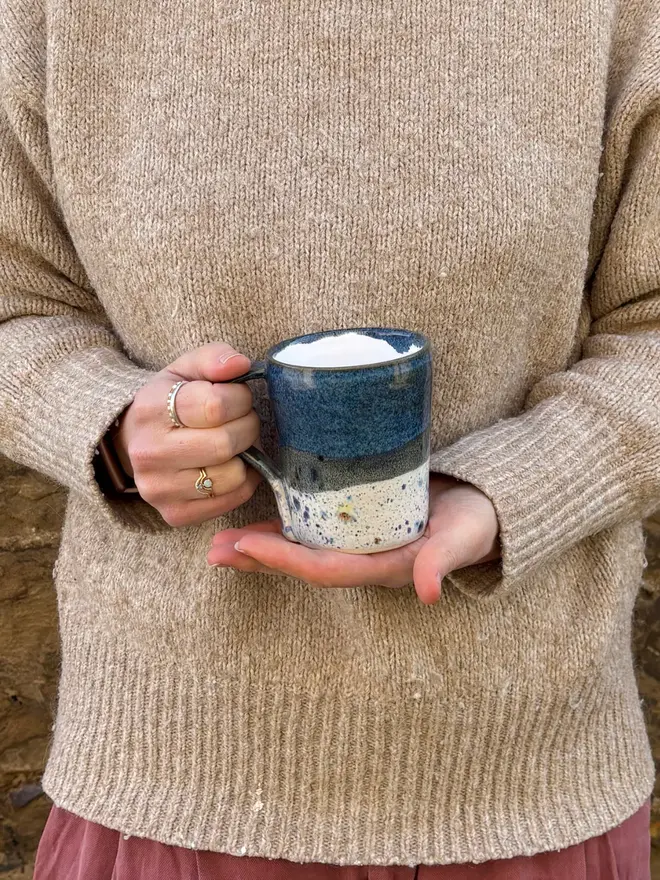 Shoreline Standard Mug, a colourful mug held in front of a person in a jumper. 