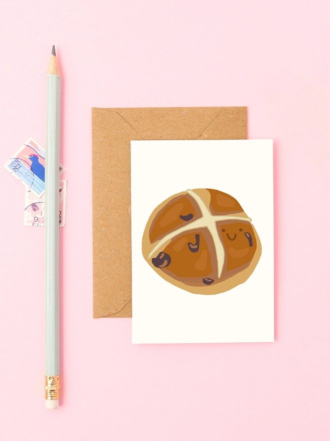 A playful hand-drawn hot cross bun with a smiley face, perfect for Easter greetings or food lovers. A small, fun card for springtime gifting.