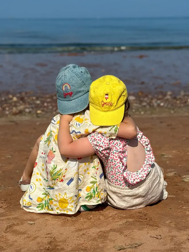 Children sit on the beach wearing hand-embroidered caps