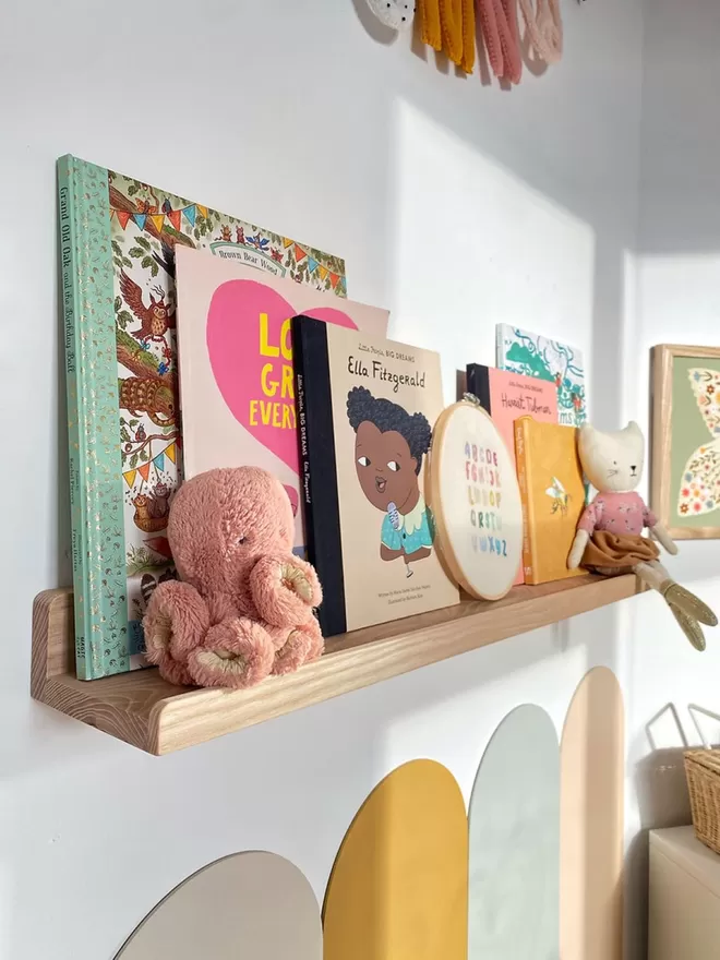 A gorgeous colourful kids room. A side view of a solid wood picture ledge shelf is styled up with kids books, teddies and children's decor.