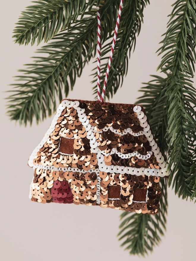 A deep golden sequinned gingerbread house hanging on a tree