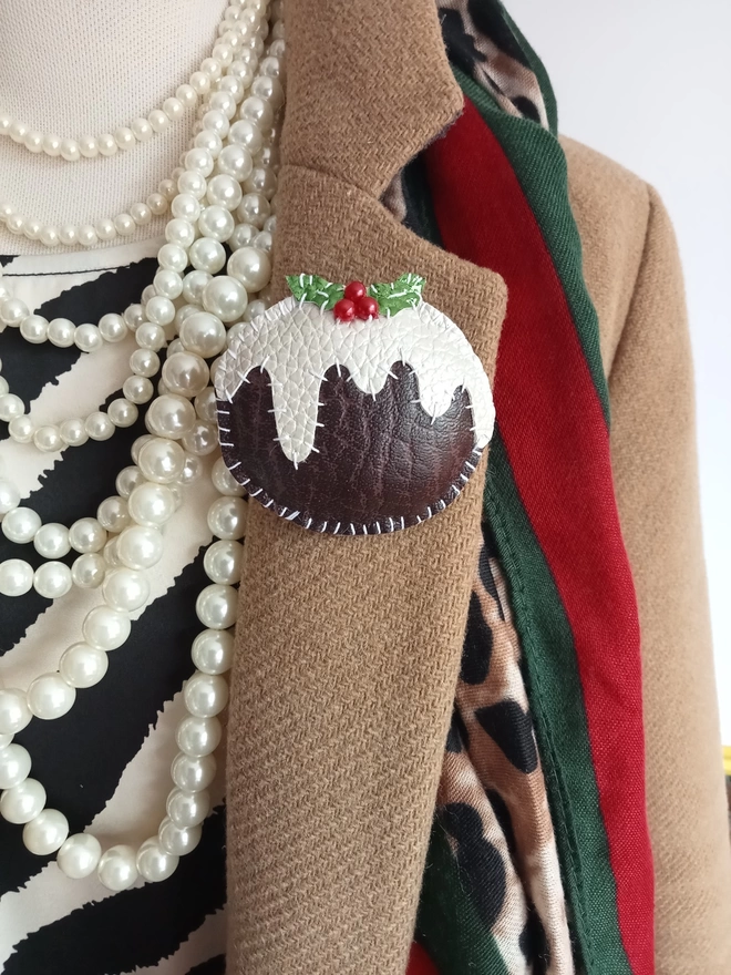 Faux leather christmas pudding brooch pinned onto a camel coat