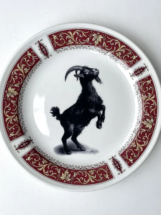 a vintage plate with an ornate border, in the centre of the plate is a vintage style black and white illustration of a Blac Phillip goat
