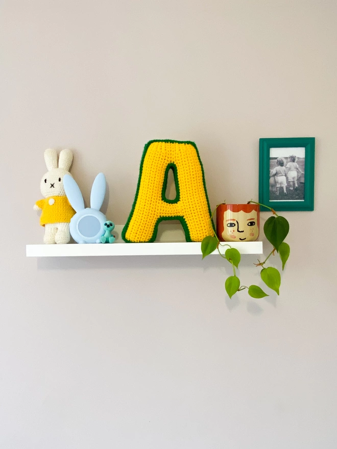 Crocheted Letter A in Sunshine Yellow and Grass Green on a shelf in a childs bedroom