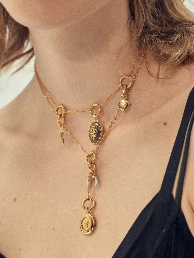 woman wearing two gold necklaces featuring a labradorite pendant, a gold locket and a mix of charms