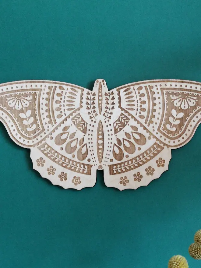 Wooden Folk Art Butterfly Hanging Decoration, wooden insect decoration hanging on a green wall. 