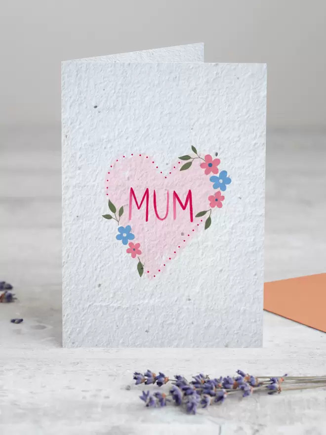 Seeded Paper Greeting Card featuring an illustration of a heart with flowers with ‘Mum’ in the centre with a sprig of Lavender placed in the foreground of the image