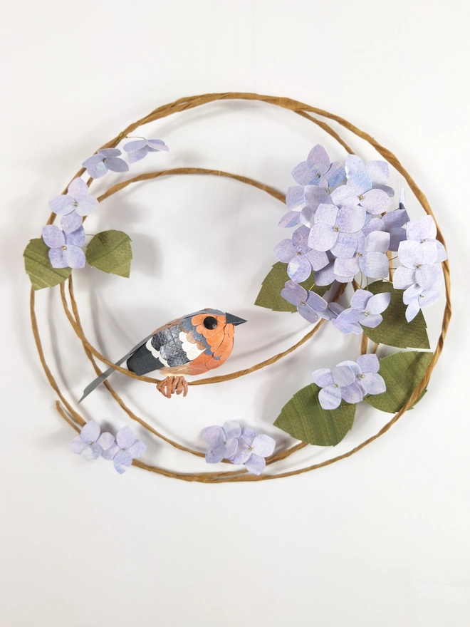 Paper sculpture wall hanging, depicting a chaffinch bird on a spring wreath of blue hydrangea flowers