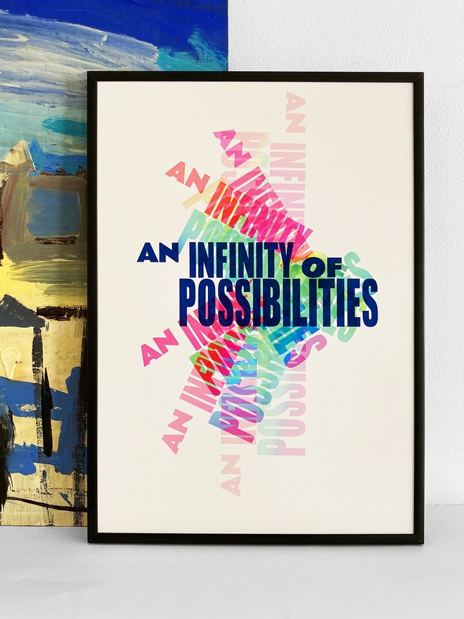 Framed multicoloured typographic print of “An Infinity Of Possibilities”  The print rests against a blue and yellow abstract painting.