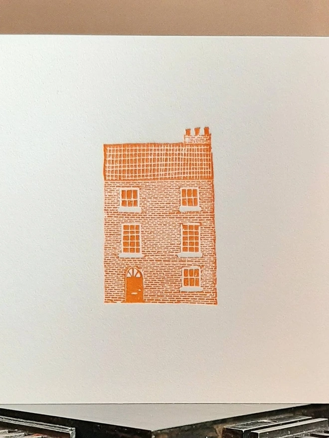 Orange Townhouse Letterpress Handprinted Greetings Card, a white card with an orange townhouse design in the centre. 