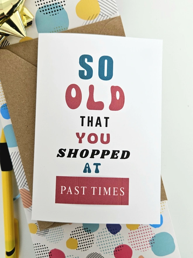 A photograph of the front of a humorous A6 greeting card illustrated using brightly coloured text and the retro shop logo. The text says so old you shopped at Past Times