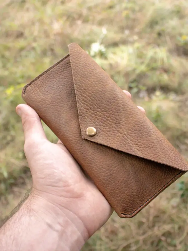 hand stitched leather pouch. a brown leather pouch held in hand against a grassy background