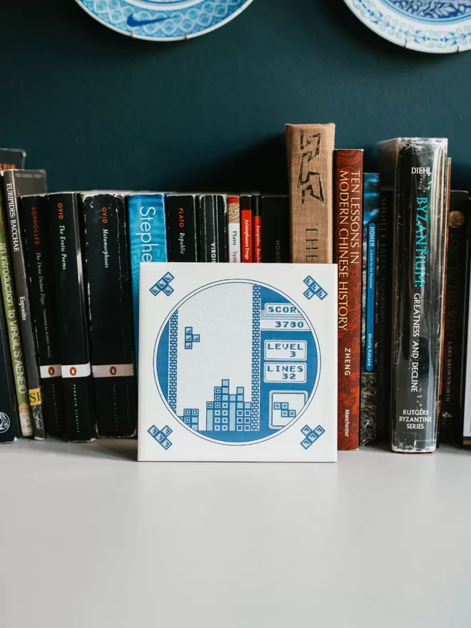 Hand Printed Delft Style Tetris Tile by Haus of Lucy seen in front of books.